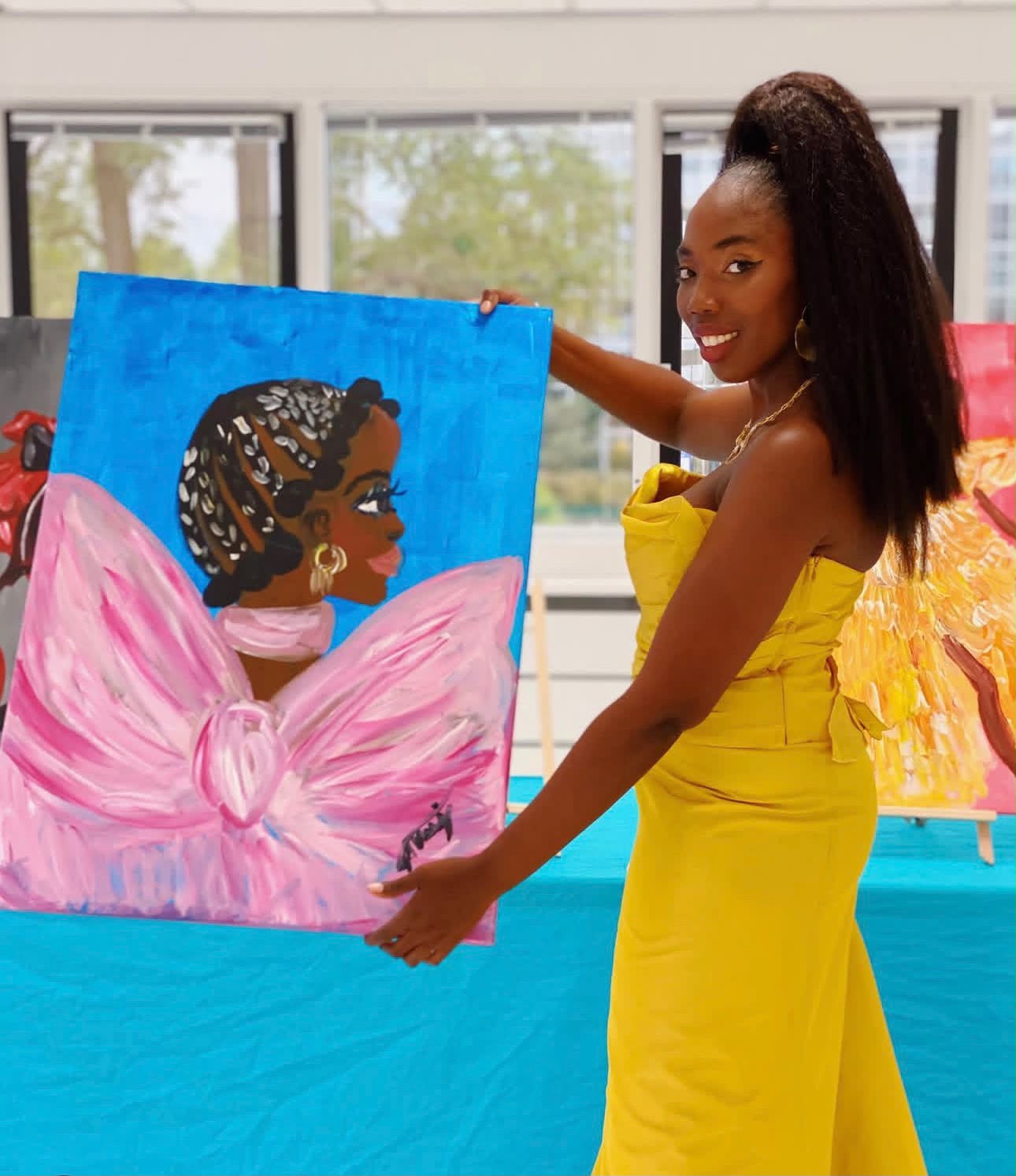 Michelle Amo holding a painting, wearing a yellow dress