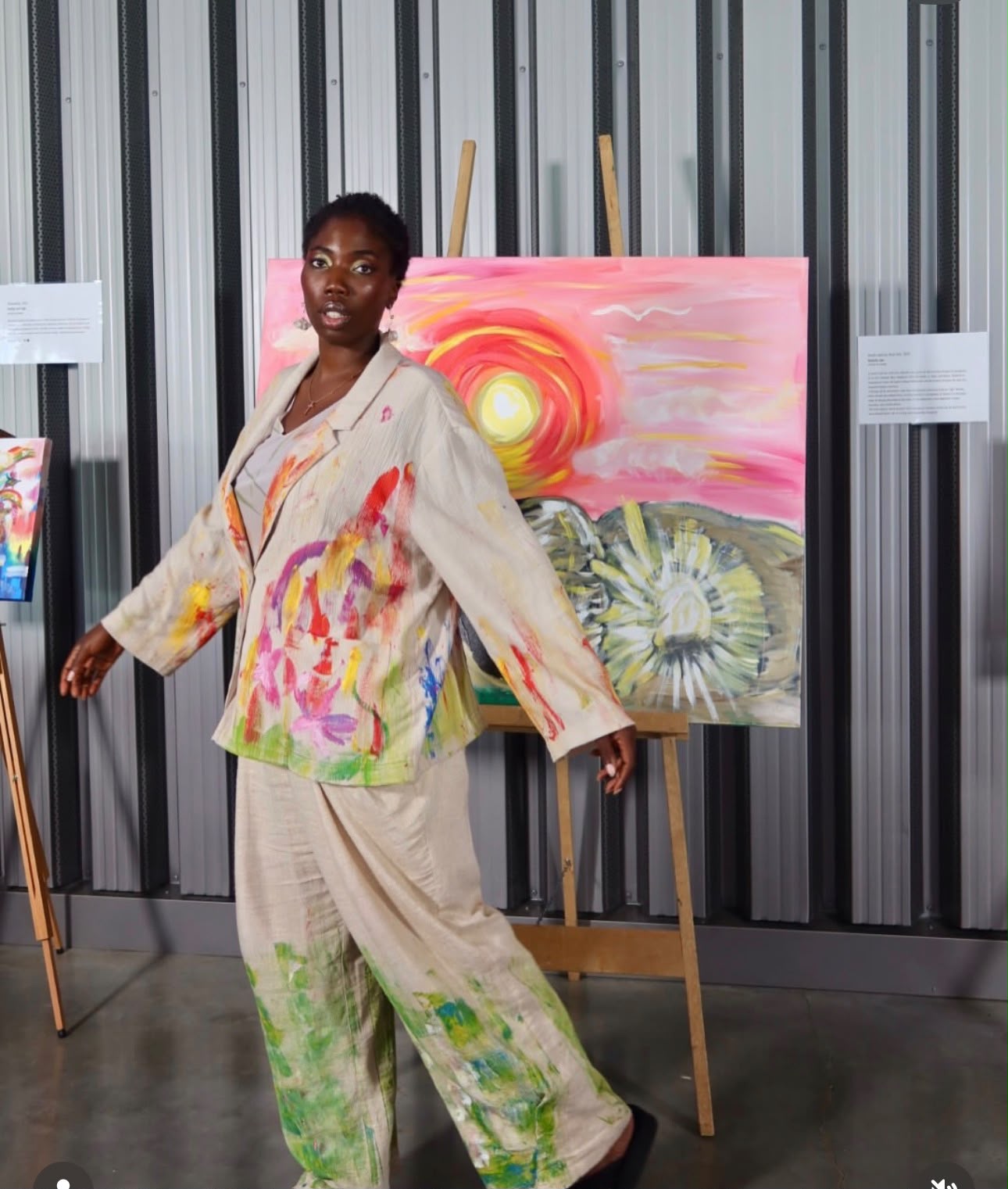 Michelle Amo in a paint-splattered suit beside a work on the easel